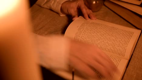 Big-Close-up-girl-magician-in-a-dark-room-with-candlelight-looking-for-a-spell-in-a-book.-Low-key-live-camera.-Mystic.-Small-DOF.-view-from-above