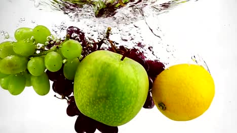 The-lemon,-apple-and-grapes-falling-in-water-with-bubbles.-Video-in-slow-motion.-Fruits-on-isolated-a-white-background.