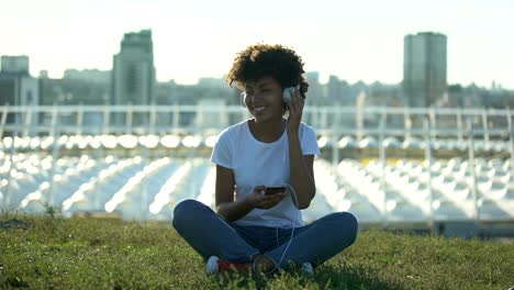 Mujer-afroamericana-joven-escuchando-música-en-auriculares,-sentado-en-el-césped,-relax