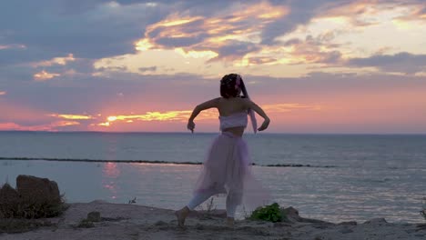 Nettes-Mädchen-mit-hellen-Make-up-in-einem-rosa-Kleid-tanzen-am-Ufer-des-Flusses.-Der-Tanz-einer-sinnlichen-Frau-mit-einer-wunderschönen-Frisur-mit-Blumen.-Slow-Motion.