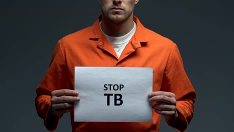 Stop-TB-phrase-on-cardboard-in-hands-of-Caucasian-prisoner,-healthcare-need