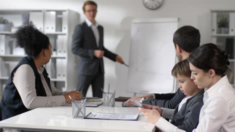 Mutter-spielt-auf-Tablet-mit-kleinem-Sohn-während-Office-Meeting