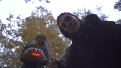 Hombre-y-dos-mujeres-jóvenes-con-trajes-de-Halloween-mirando-hacia-abajo-en-la-víctima-con-caras-de-miedo-serioenentes-en-el-parque-de-otoño