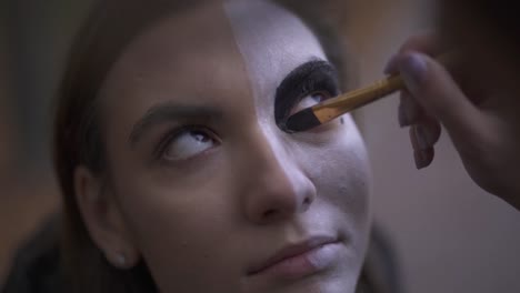 Makeup-artist-doing-Halloween-makeup-on-the-face-of-a-beautiful-girl-using-brush-close-up.