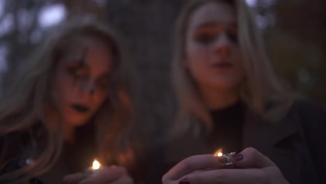 Two-young-blonde-girls-with-terrifying-Halloween-makeup-holding-small-candles-in-hands-and-looking-at-the-camera.