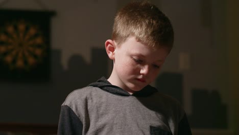 Sad-young-boy-standing-in-his-room-alone-and-looking-down