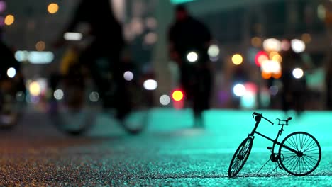 Lot-of-cyclists-ride-during-night-cycling-bike-parade-in-blur-by-illuminated-night-city-street-against-background-of-small-scale-model-of-bicycle.-Crowd-of-people-on-bike.-Bike-traffic.-Concept-sport-healthy-lifestyle.-Bright-shining-lights.-Low-angle