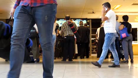 People-looking-at-timetable-departure-board-at-international-airport.-Passengers-with-luggage-walking-in-the-terminal.-Timelaps