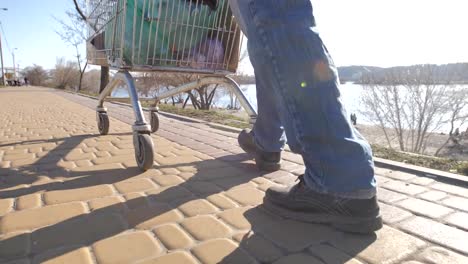 Rear-view-of-homeless-man's-legs-walking-with-cart