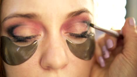 Make-up-artist-puso-en-sombras-en-un-párpado.-Modelo-de-pelo-claro.-Vista-de-cerca.-Parches-de-ojos-ahumados,-oro-debajo-de-ojos