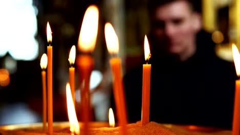 The-man-looks-at-the-burning-candles-in-the-focus,-slow-motion