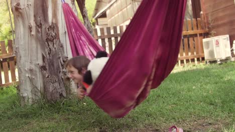 Joven-niña-feliz-en-el-campamento-de-verano-en-coloridas-hamacas-relajantes-jugando-afuera-con-muñecas-de-panda-de-felpas-en-la-hierba-verde-campo-niños-niños-lenta