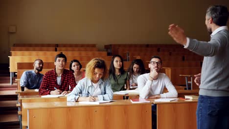 Ernster-Mann-High-School-Lehrer-ist-im-Gespräch-mit-Studenten-dann-junger-Kerl-in-Gläsern-Hand-auslöst-und-Frage.-Bildung,-Vortrag-und-College-Konzept.