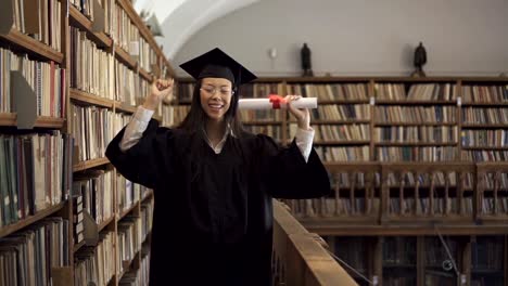 Attractive-student-in-academic-dress-is-having-fun,-standing-in-library