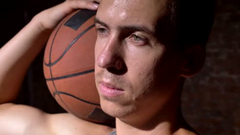 Serious-basketball-player-holding-ball-on-his-shoulder-and-looking-sideways