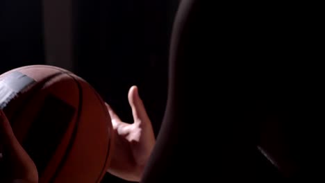 Basketball-player-sitting-and-holding-ball,-waiting-to-for-game-to-start,-dark-room-background