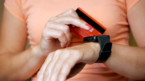 Woman-buying-online-with-credit-card-on-smart-watch.-Consumerism-internet-online-purchases.-Girl-is-Paying-with-a-Smart-Watch.-Online-shopping-with-smartwatch-and-a-credit-card-in-hand.