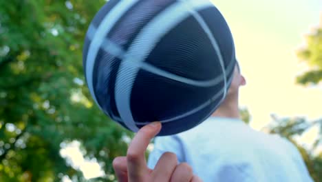 Young-man-spinning-basketball-on-one-finger-in-park,-outdoor-court,-low-angle