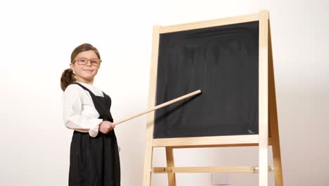 A-happy-girl-dressed-as-a-teacher-in-front-of-a-small-blackboard-holds-her-arms-folded-and-smiles.