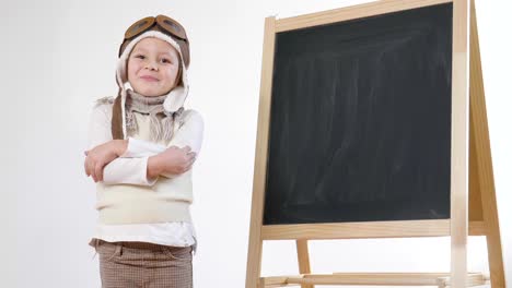 Una-pequeña-niña-vestida-como-un-aviador-o-piloto,-indica-con-su-mano-la-pizarra-detrás-de-ella-como-un-iniciar-vuelo-para-aprender-a-usar-el-avión-y-la-imaginación.