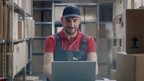 Worker-Uses-Laptop-while-Sitting-at-His-Desk-in-the-Warehouse.