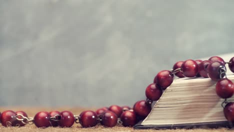 Open-Bible-and-the-crucifix-beads-on-a-golden-table,-close-up.-Beautiful-dark-background.-Religion-concept