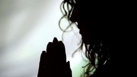 Close-up-of-woman-holding-hands-in-prayer-asking-God-to-help,-praying-silhouette