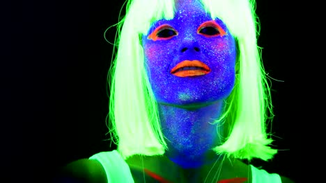 Woman-with-UV-face-paint,-wig,-glowing-clothing-dancing-in-front-of-camera,-face-close-up-of-make-up.-Caucasian-woman.-.