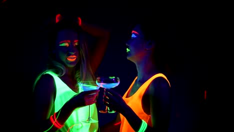 Women-with-UV-face-paint,-laser,-glowing-bracelets,-drinks,-glowing-clothing-dancing-together-in-front-of-camera,-Half-body-shot.-Caucasian-and-asian-woman.-.