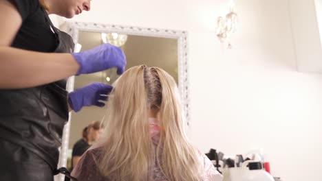 A-close-up-of-a-hairdresser-standing-to-the-left-of-the-blonde-and-taking-dyed-strands-one-by-one.-The-bottom-view.