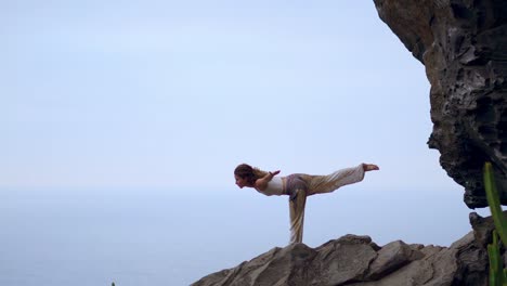 Woman-meditating-in-yoga-warrior-pose-at-the-ocean,-beach-and-rock-mountains.-Motivation-and-inspirational-fit-and-exercising.-Healthy-lifestyle-outdoors-in-nature,-fitness-concept.