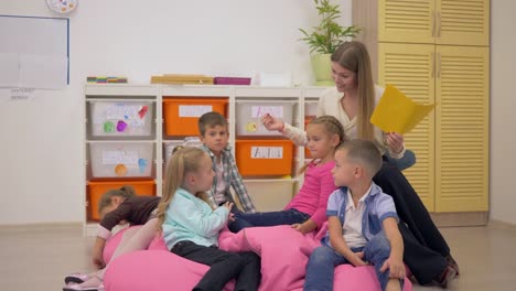 maestra-agradable-sentarse-en-la-silla-del-bolso-de-haba-y-hablar-con-los-niños-en-clase-en-la-escuela