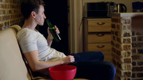 Man,-football-fan-is-drinking-beer-and-chips-in-front-of-TV