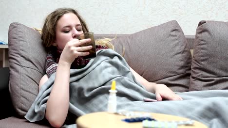 Teen-girl-drinking-medicine-tea-warm.-Lying-on-the-couch,-covered-with-a-blanket