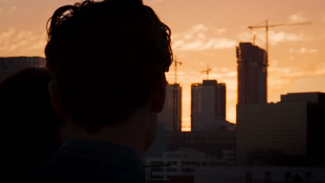 Rückansicht-des-Paares-auf-auf-dem-Dachterrasse-mit-Blick-über-Stadt-Skyline-bei-Sonnenuntergang