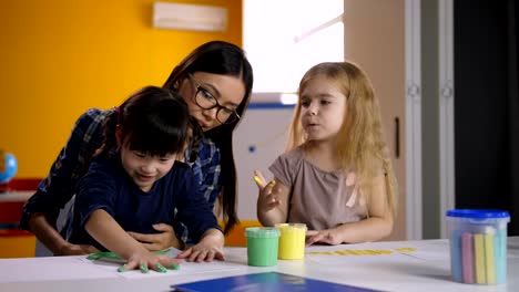 Diverse-kids-with-teacher-hand-painting-in-class