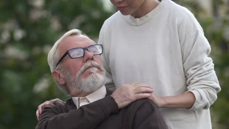 Woman-carrying-disabled-man-in-wheelchair,-caring-for-seriously-ill-patient