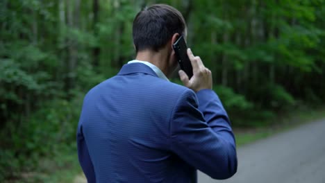 gut-aussehender-Mann-zu-Fuß-entlang-der-Straße-im-Wald,-am-Telefon,-Blick-zurück