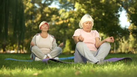 Elder-women-sitting-in-lotus-position-and-meditating-doing-yoga-in-park,-energy