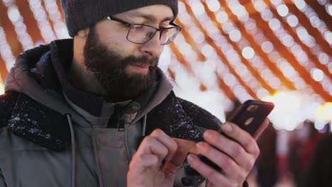 Bearded-man-use-smartphone-app,-Christmas-lights.-Close-up-shot