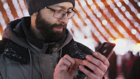 Hombre-barbudo-usar-aplicación-para-smartphone,-luces-de-Navidad.-Primer-plano-tiro