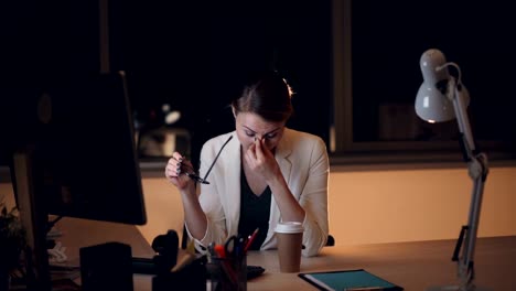 Müde-Blondine-in-Gläsern-und-Anzug-ist-spät-in-der-Nacht-am-Computer-arbeiten-und-Take-out-Kaffeetrinken-müde-und-erschöpft-fühlen.-Job,-Übermüdung-und-Getränke-Konzept.