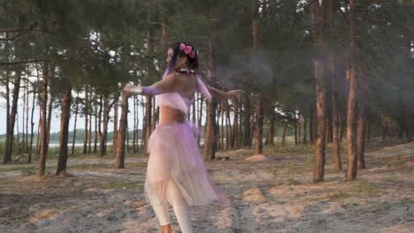 Señora-hermosa-con-maquillaje-brillante-en-un-vestido-rosado-bailando-con-bombas-de-humo-en-el-fondo-de-los-pinos.-El-baile-de-una-mujer-sensual-con-un-peinado-de-flor.-Cámara-lenta.