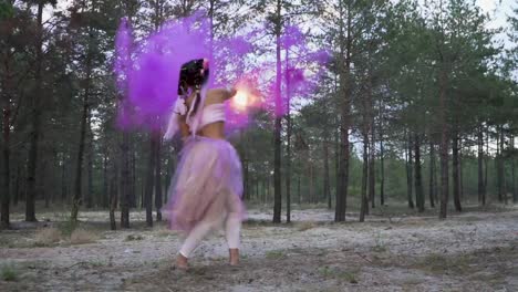 Tender-woman-with-bright-makeup-in-a-pink-dress-dancing-with-burning-smoke-bombs-on-the-background-of-pine-trees.-The-dance-of-a-sensual-girl-with-a-wonderful-hairstyle-with-flowers.-Slow-motion.