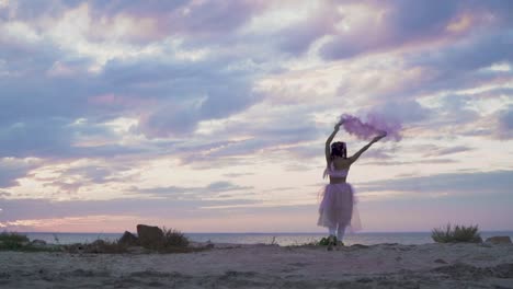 Tierna-chica-con-maquillaje-brillante-en-un-vestido-rosado-bailando-con-bombas-de-humo-en-la-orilla-del-río.-El-baile-de-una-mujer-sensual-con-un-peinado-maravilloso-con-flores.-Cámara-lenta.