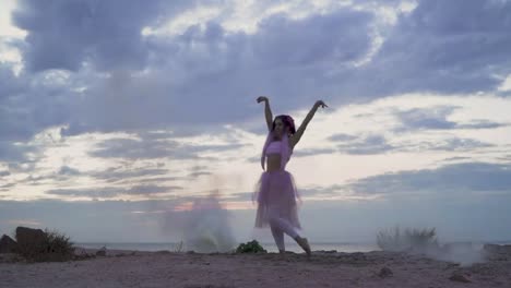 Hermosa-chica-con-maquillaje-brillante-en-vestido-rosa-bailando-en-la-niebla-de-bombas-de-humo-en-la-orilla-del-río.-El-baile-de-una-mujer-sensual-con-un-peinado-de-flor.-Cámara-lenta.