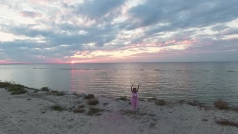 Atop-view-of-sensual-young-woman-with-sparkling-makeup-in-a-pink-dress-dancing-with-smoke-bombs-on-the-bank-of-the-river.-The-dance-of-a-pretty-sweet-girl.-Slow-motion.-Shooting-from-the-drone.