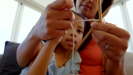 Vista-de-ángulo-bajo-de-negro-madre-enseñando-a-su-hija-que-hace-punto-en-una-cómoda-casa-4k