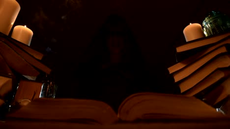 Close-up-of-a-bored-girl-magician-in-a-dark-room-in-candlelight-dabbles-in-a-book-and-meditates.