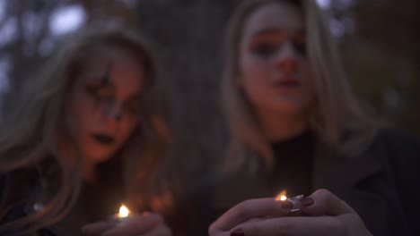 Retrato-de-dos-chicas-con-maquillaje-de-Halloween-en-rostros-sosteniendo-pequeñas-velas-en-las-manos-mirando-en-la-cámara.